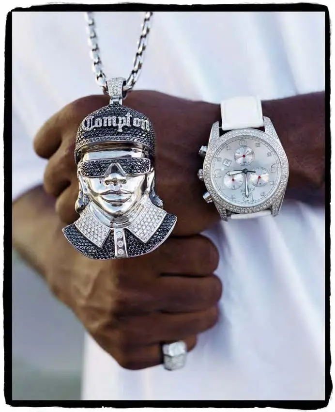 Photograph of Little Ez fists in front of a white t-shirt, presenting a large silver pendant and watch.