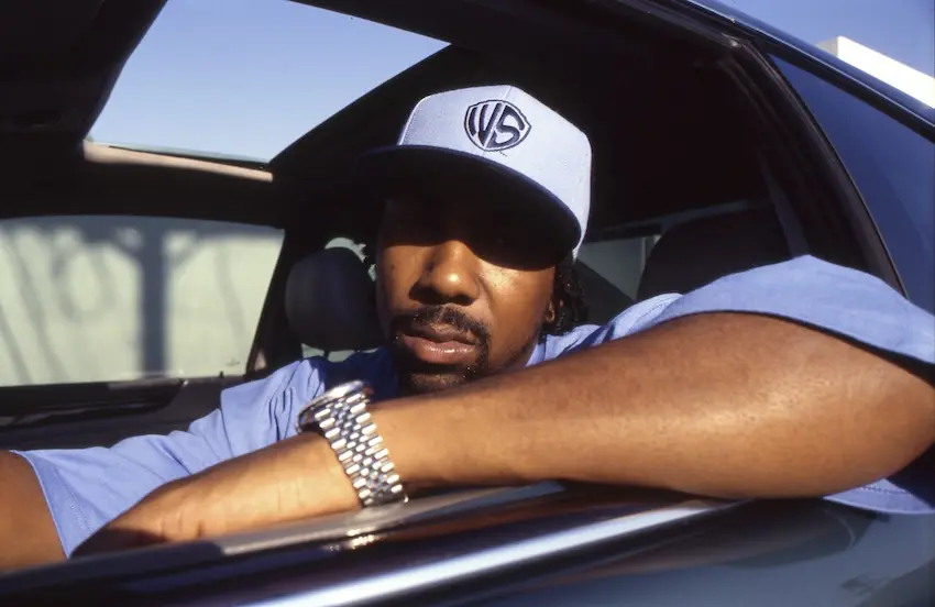 Photograph of West Side MC Eight leaning out of a car window, dressed with a cap and large silver watch