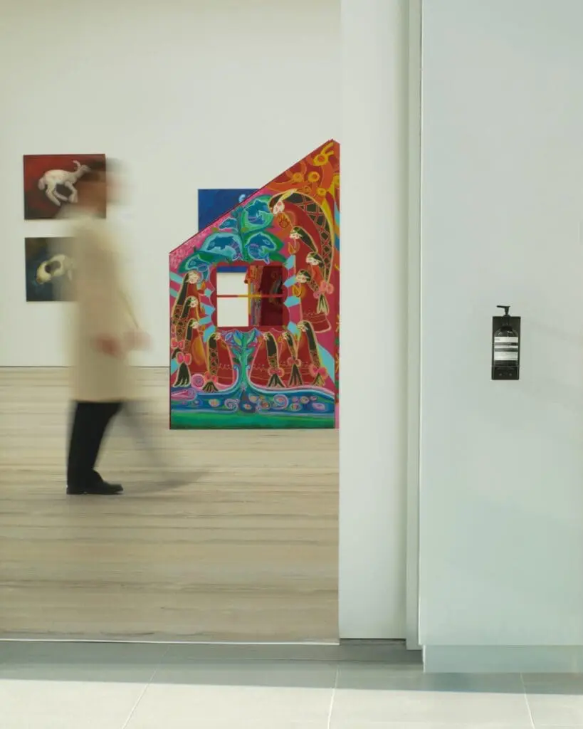 Aesop hand cream in front of an exhibition room at Saatchi Gallery, with a blurred figure walking past a bright res and yellow house sculpture