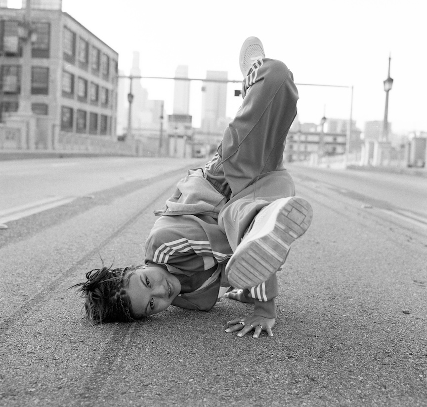 Black and white photograph of a young boy breakdancing in the street